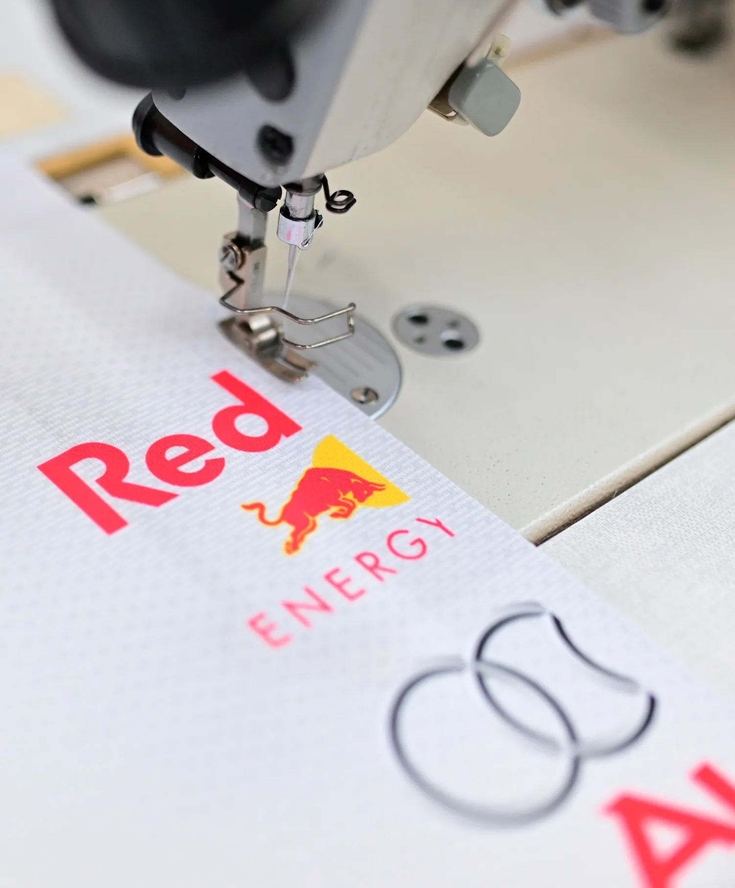 En syemaskin syr en hvit sportstøy med Red Bull Energy-logo.