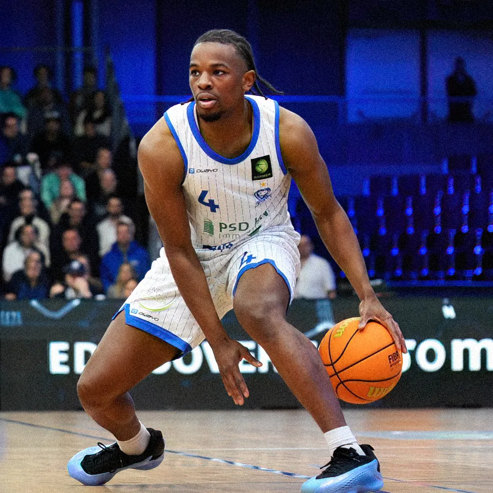 En basketballspiller dribler ballen på banen mens han har på seg en stripete drakt med nummer 4.